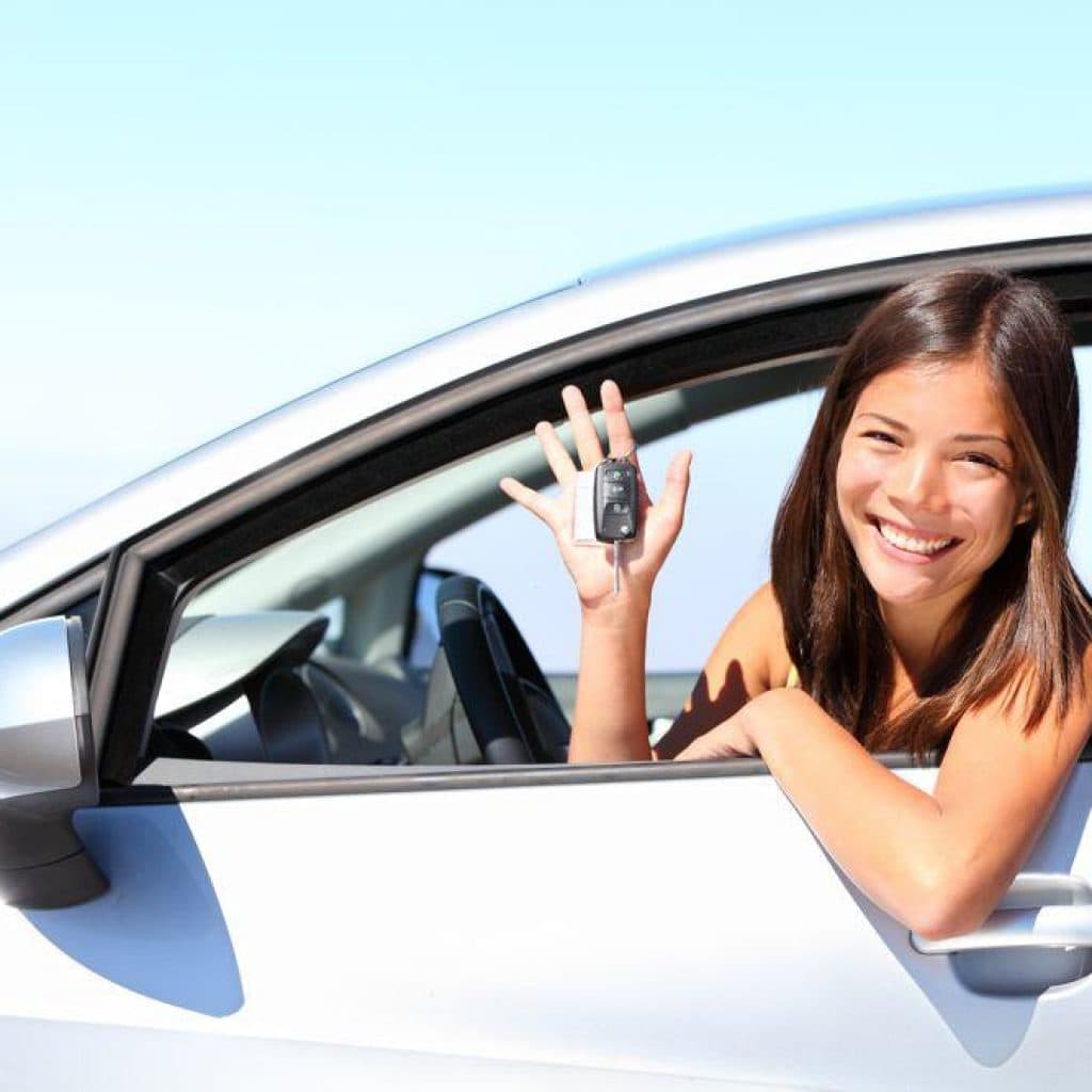 Car loan woman with key in hand waves out of car