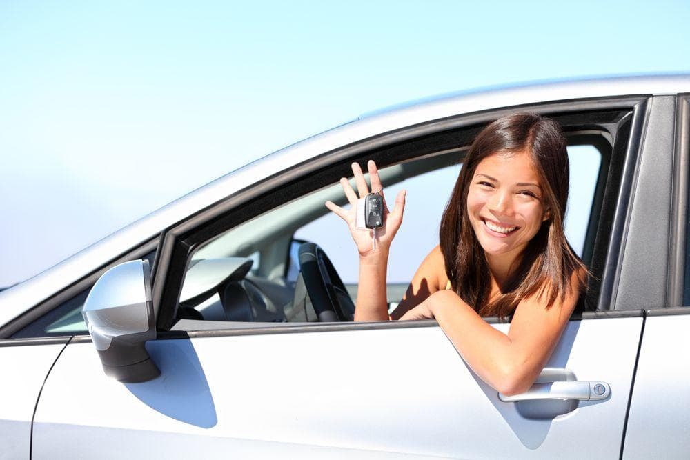 Mujer de préstamo de coche con la llave en la mano saluda fuera del coche