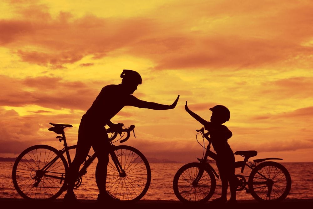 Crédito pela bicicleta ou bicicleta pai mexericando com criança ao pôr-do-sol